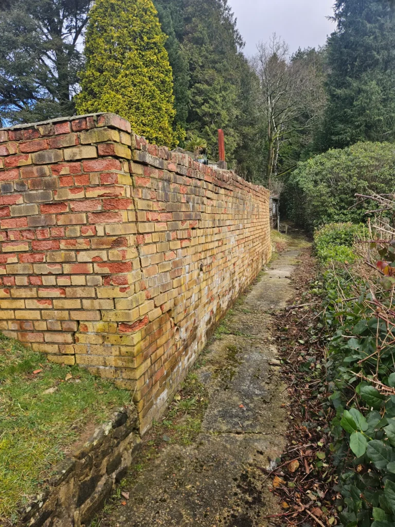 Brick boundary wall along a narrow path following repair or repointing work.