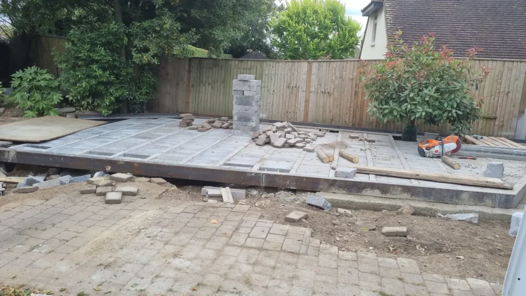 Patio area under construction with paving slabs being positioned on a prepared base.