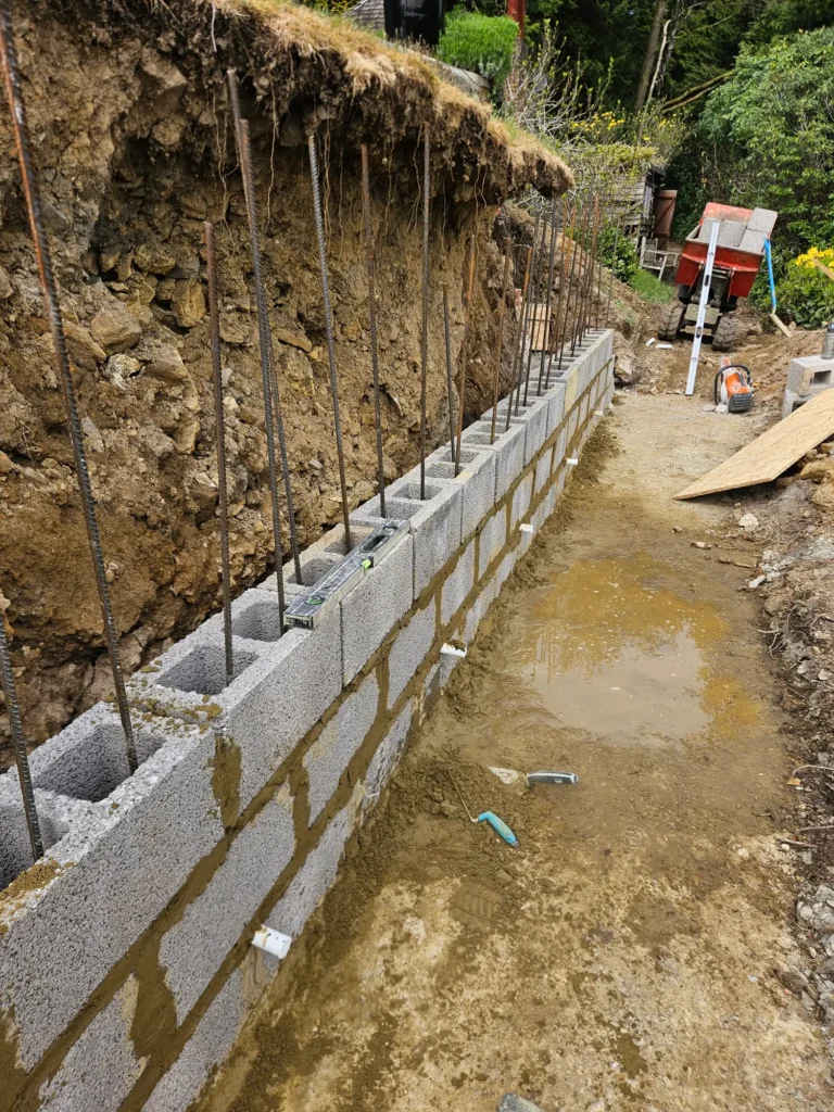 Blockwork retaining wall under construction along an excavated boundary.